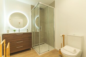 A modern bathroom with a glass-enclosed shower, a wooden vanity with a mirror, and a toilet. - Cravo Studio by Atlantic Holiday (Santa Cruz)