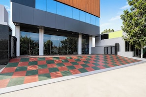 A modern building with a checkered floor pattern, large windows, and a tree in the background.