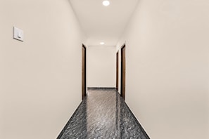 A hallway with a marble floor, white walls, and wooden doors.