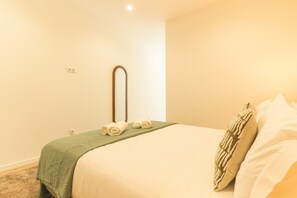 A hotel room with a bed, a green throw blanket, two rolled towels, a wooden mirror, and a wall socket. - Estrelicia Studio by Atlantic Holiday (Santa Cruz)