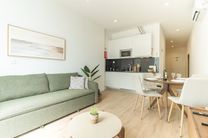 A modern living space with a green sofa, a dining table with chairs, and a kitchen area with a microwave. - Estrelicia Studio by Atlantic Holiday (Santa Cruz)