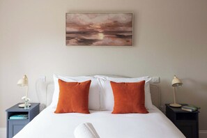 A neatly made bed with white linens and two orange pillows, flanked by two bedside tables with lamps and books. - Spacious Sidlesham Country Home near Witterings (Sidlesham)