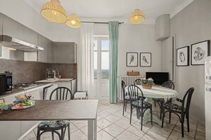A modern kitchen with a dining area, featuring a large window, pendant lights, and framed artwork on the wall.