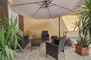 An outdoor seating area with wicker furniture, a large umbrella, and potted plants.