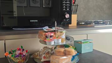 A kitchen with a microwave, a gas stove, and a glass display stand with snacks and tea.