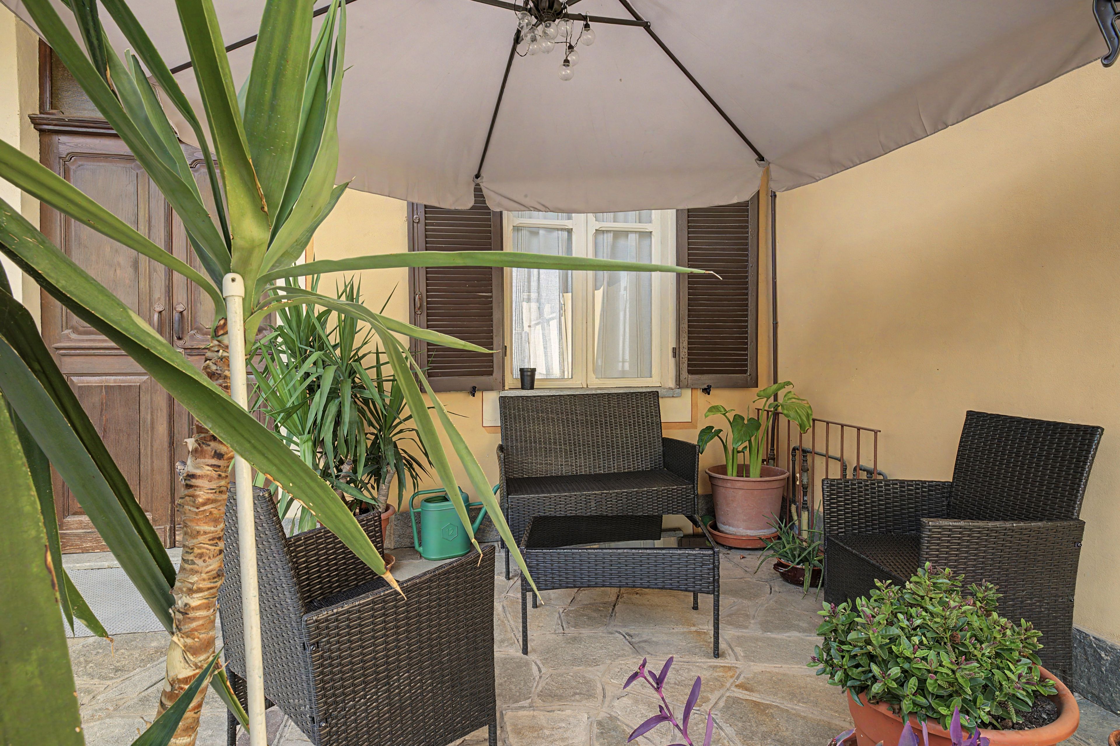 Un patio cubierto con mobiliario de mimbre, plantas en macetas y piso de piedra.