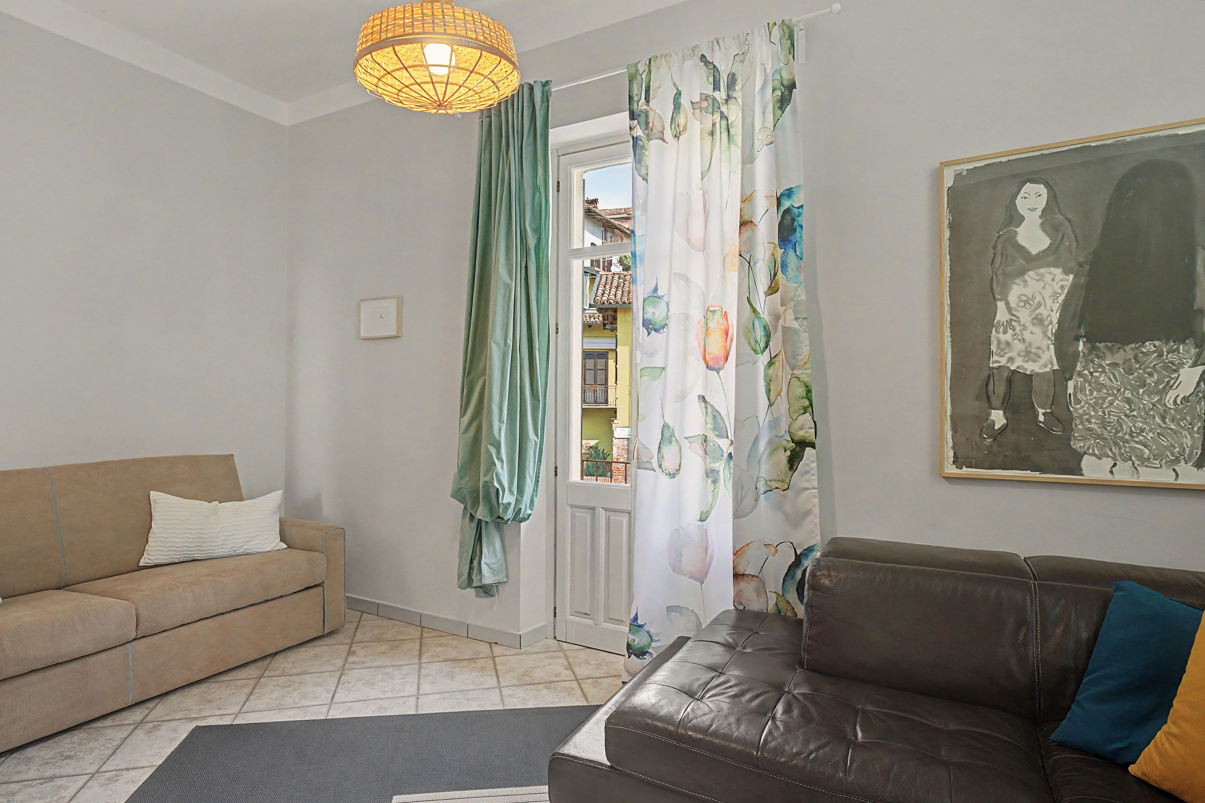 Una sala de estar con un sofá, un sofá de cuero marrón, un tapete, un cuadro y una ventana con cortinas.