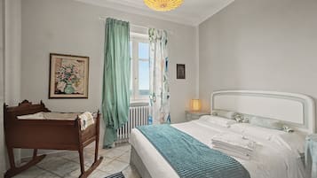 Et soveværelse med en seng, en træbænk, en radiator, et vindue med gardiner og et billede hængt på væggen.