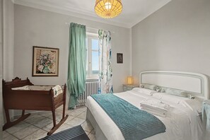 A bedroom with a bed, a wooden bench, a radiator, a window with curtains, and a wall-mounted picture.