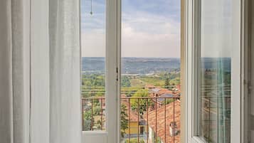 Blick aus einem Fenster mit Vorhängen auf eine Landschaft mit Gebäuden und Grünpflanzen.