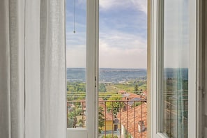 Vista des d'una finestra amb cortines, sobre un paisatge amb edificis i vegetació.