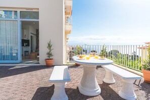 Ein Balkon mit Tisch und Bänken, einem Blumentopf und Blick aufs Meer.