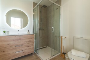 Ein modernes Badezimmer mit einer gläsernen Duschkabine, einem hölzernen Waschtisch mit rundem Spiegel und einer Toilette mit Holz-Bidet.