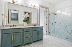 A bathroom with a large mirror, two sinks, a vase with flowers, and a glass shower enclosure.