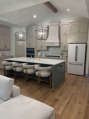 Una cocina moderna con una isla central, taburetes de bar y un refrigerador empotrado.