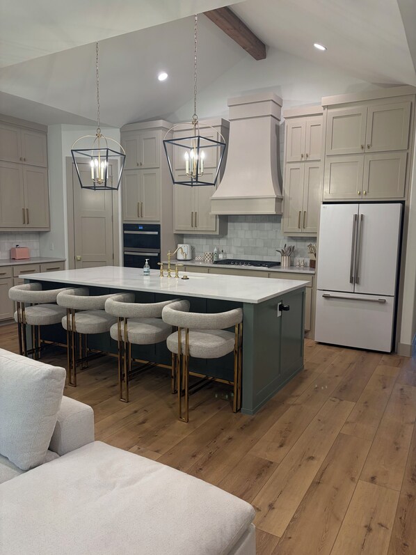 A modern kitchen with a central island, bar stools, and a built-in refrigerator.