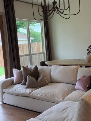 A living room with a beige sectional sofa, a chandelier, and a dining table.