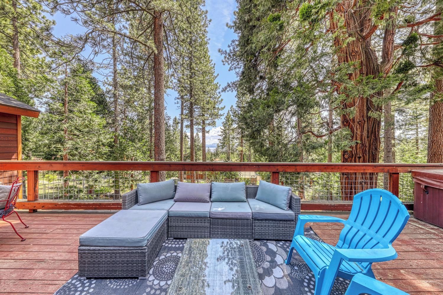 A deck with a wicker sofa and blue chairs, overlooking a forest.