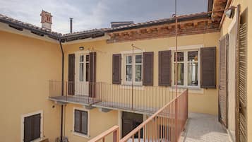 En boligbygning med balkon, trappe og flere vinduer med skodder.