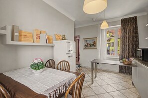 Un comedor con una mesa, sillas y una planta en maceta. Se observa un refrigerador y un microondas al fondo.