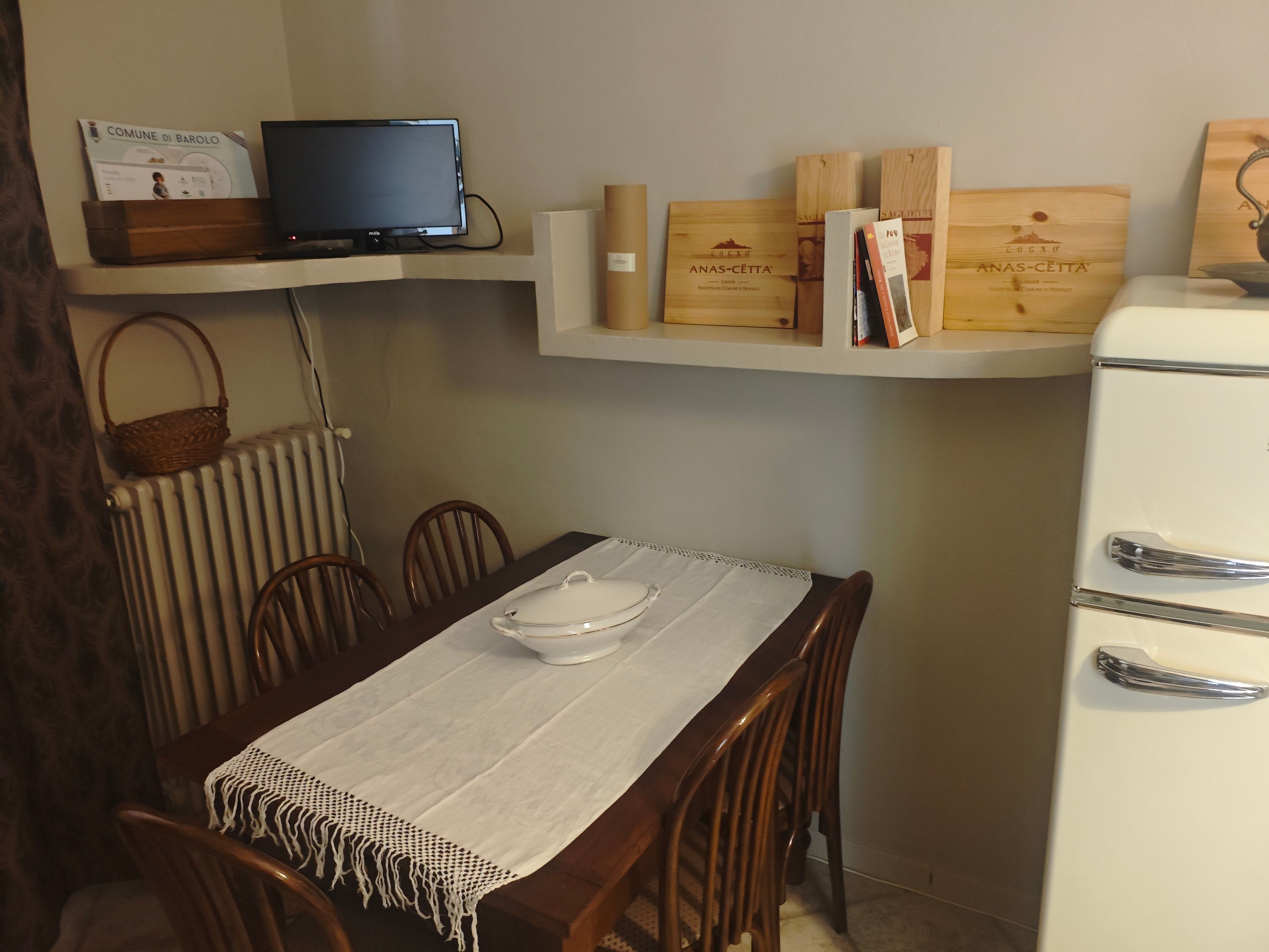 A dining area with a table set for four, a television on a shelf above, and wine boxes on a lower shelf.
