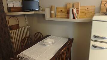 A dining area with a table set for four, a television on a shelf above, and wine boxes on a lower shelf.