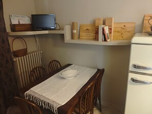 Un comedor con una mesa lista para cuatro personas, un televisor en un estante superior y cajas de vino en un estante inferior.
