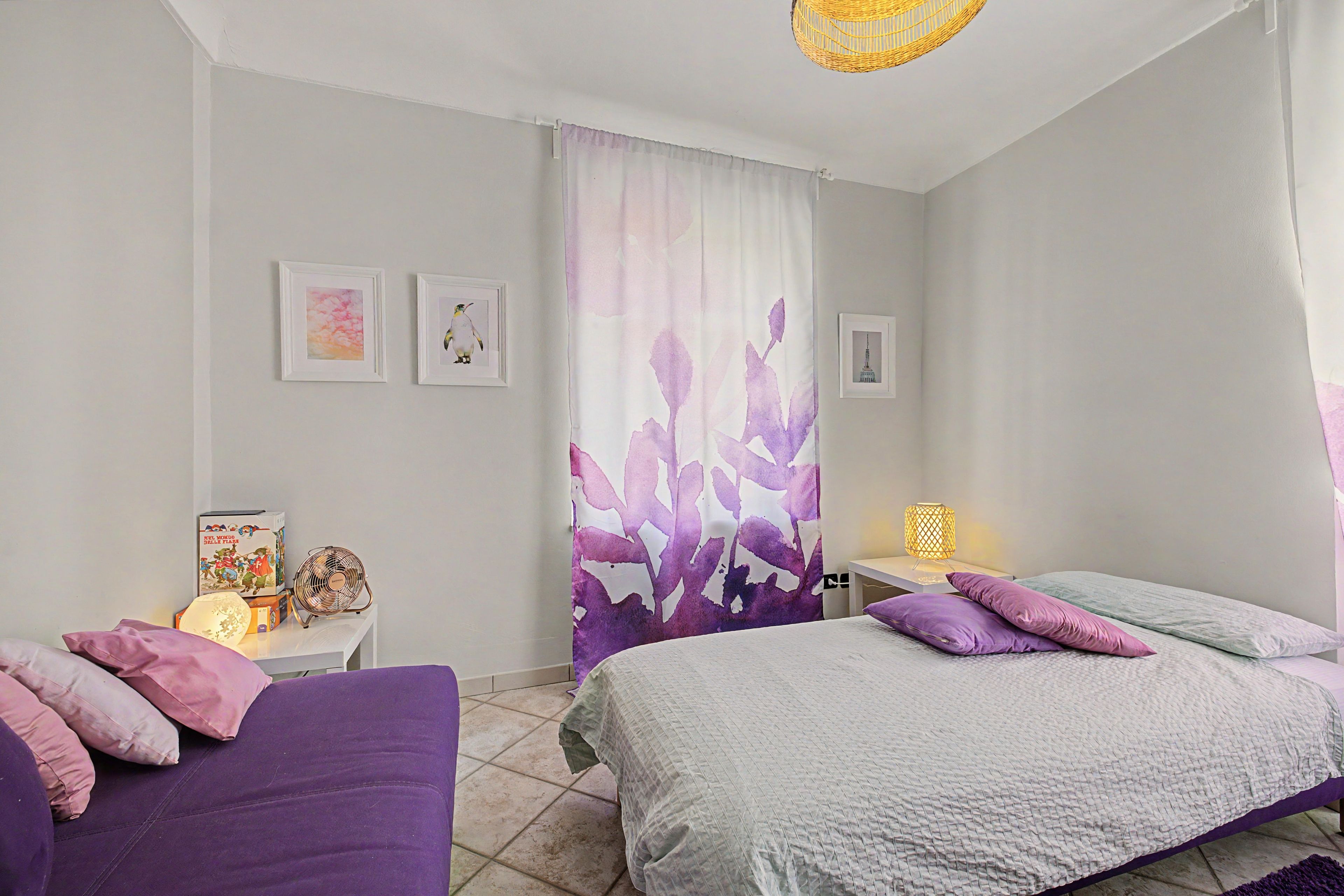 Une chambre avec deux lits, une table de chevet avec une lampe, un ventilateur et des œuvres d’art accrochées au mur.