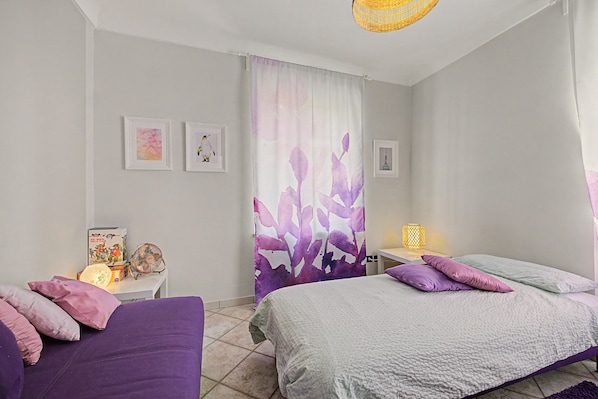 Un dormitorio con dos camas, una mesita de noche con lámpara, un ventilador y una obra de arte en la pared.
