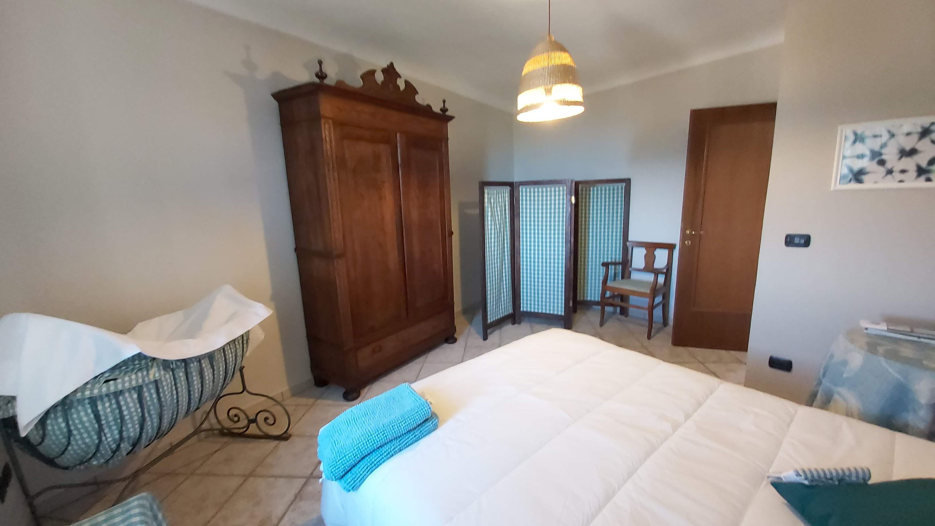A bedroom with a large bed, a wooden wardrobe, a chair, and a baby crib.