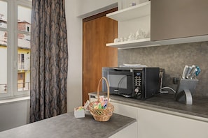 A modern kitchen with a microwave, a basket of groceries, and a window with curtains.
