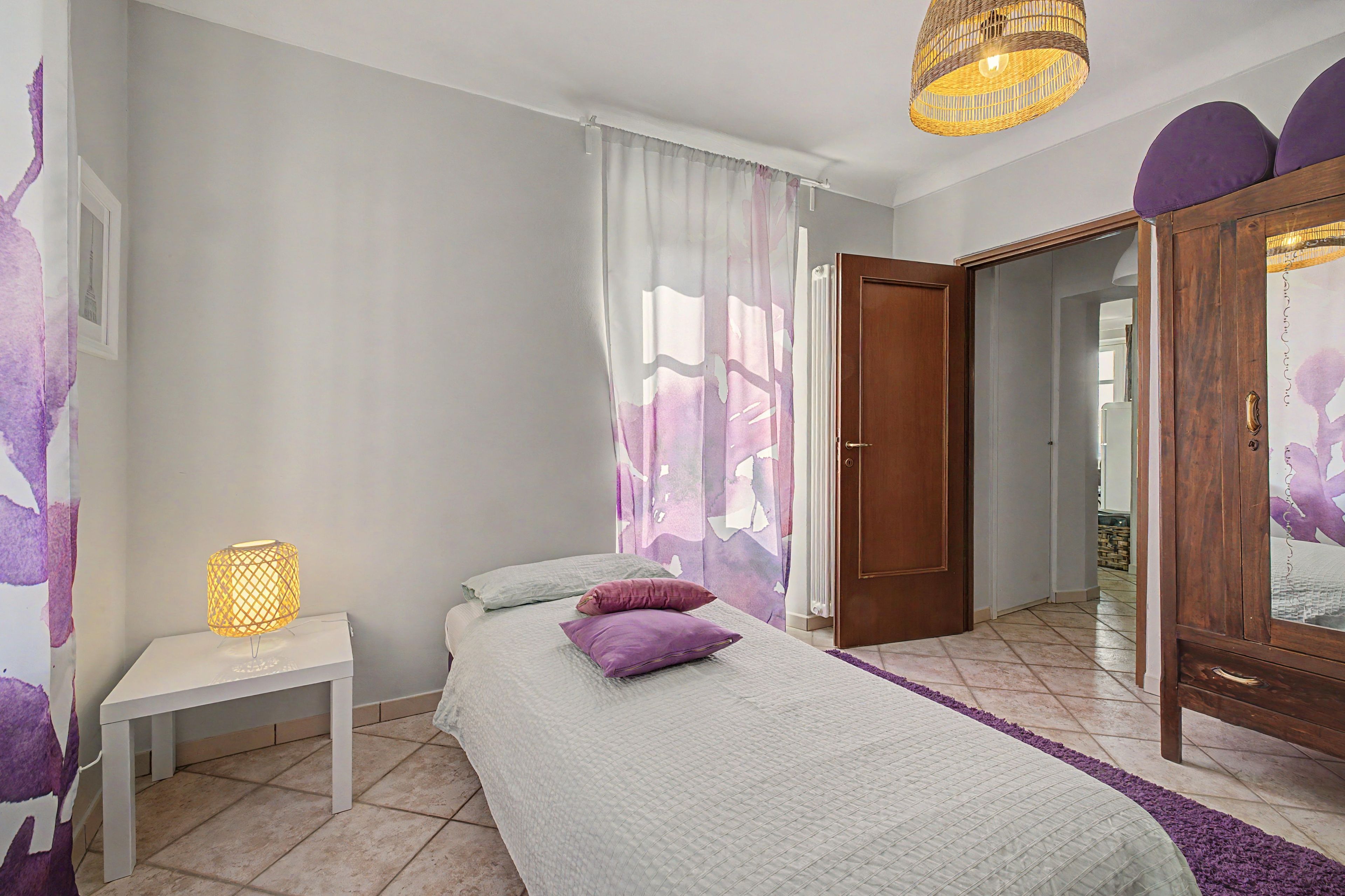Quarto com cama, mesa de cabeceira com abajur, porta e guarda-roupa.