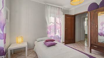 Quarto com cama, mesa de cabeceira com abajur, porta e guarda-roupa.