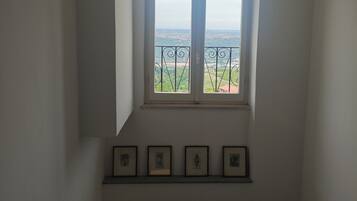 Ein Zimmer mit Fensterblick auf eine Landschaft, einer Treppe und mehreren gerahmten Bildern an der Wand.