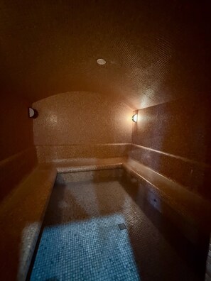 A dimly lit, tiled room with a bench and a small pool. - Studio 45 Apartment in Tsaghkadzor (Tsaghkadzor)