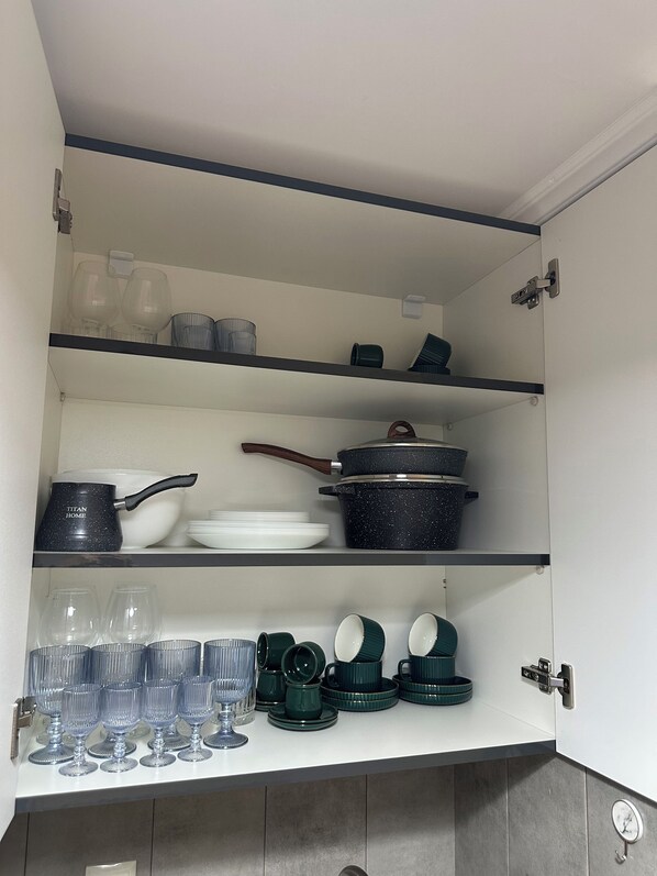A kitchen cabinet with shelves containing various kitchenware, including glassware, plates, and cookware.