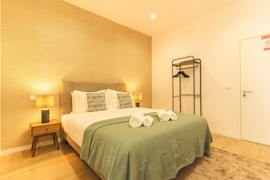 A neatly arranged hotel room with a bed, two bedside lamps, a towel rack, and a door with a sign. - Estrelicia Studio by Atlantic Holiday (Santa Cruz)