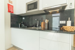 A modern kitchen with a built-in microwave, stainless steel range hood, and a granite countertop. - Estrelicia Studio by Atlantic Holiday (Santa Cruz)