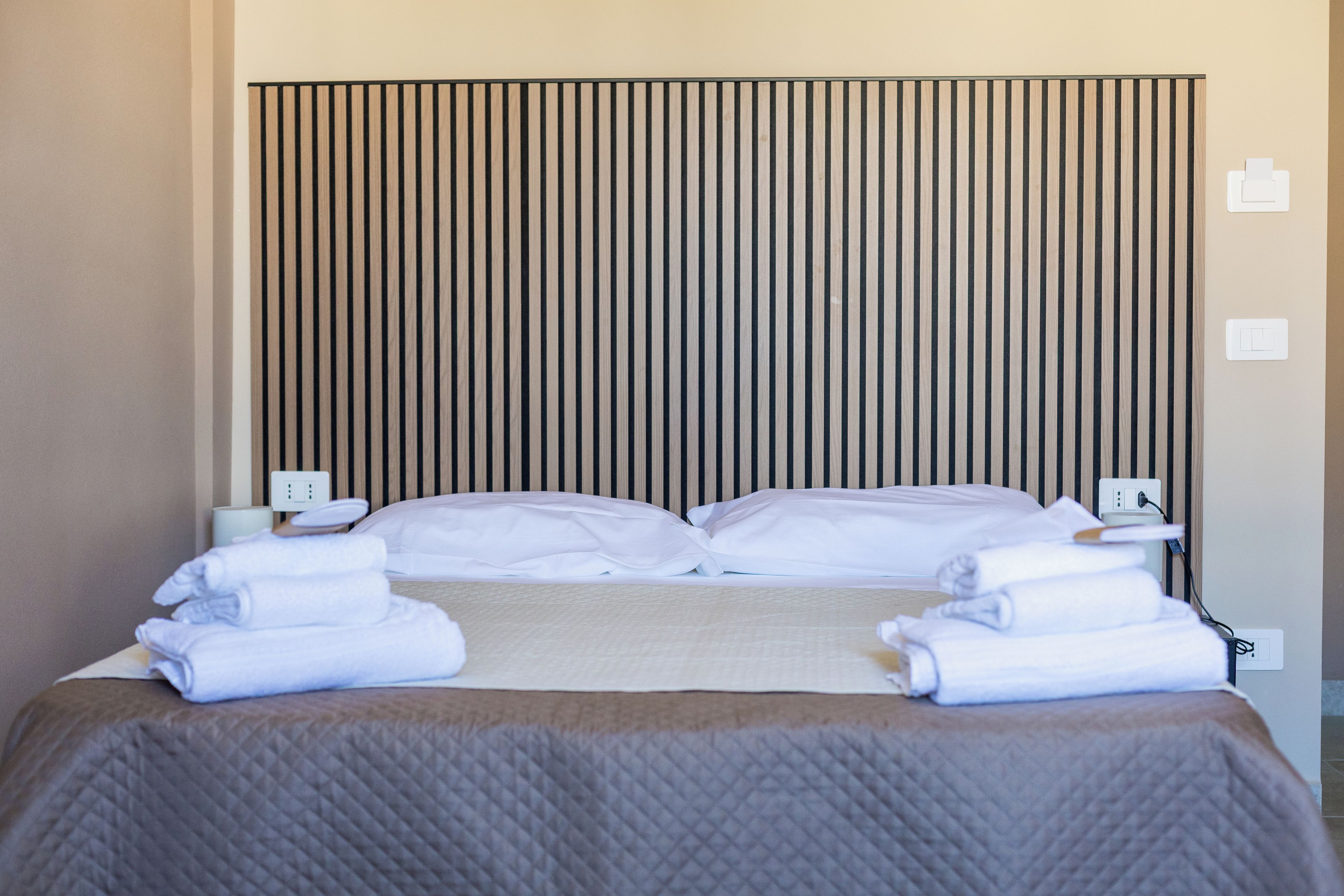 A hotel room with a bed, pillows, a blanket, and towels. There are two bedside tables with lamps and a power outlet on each.
