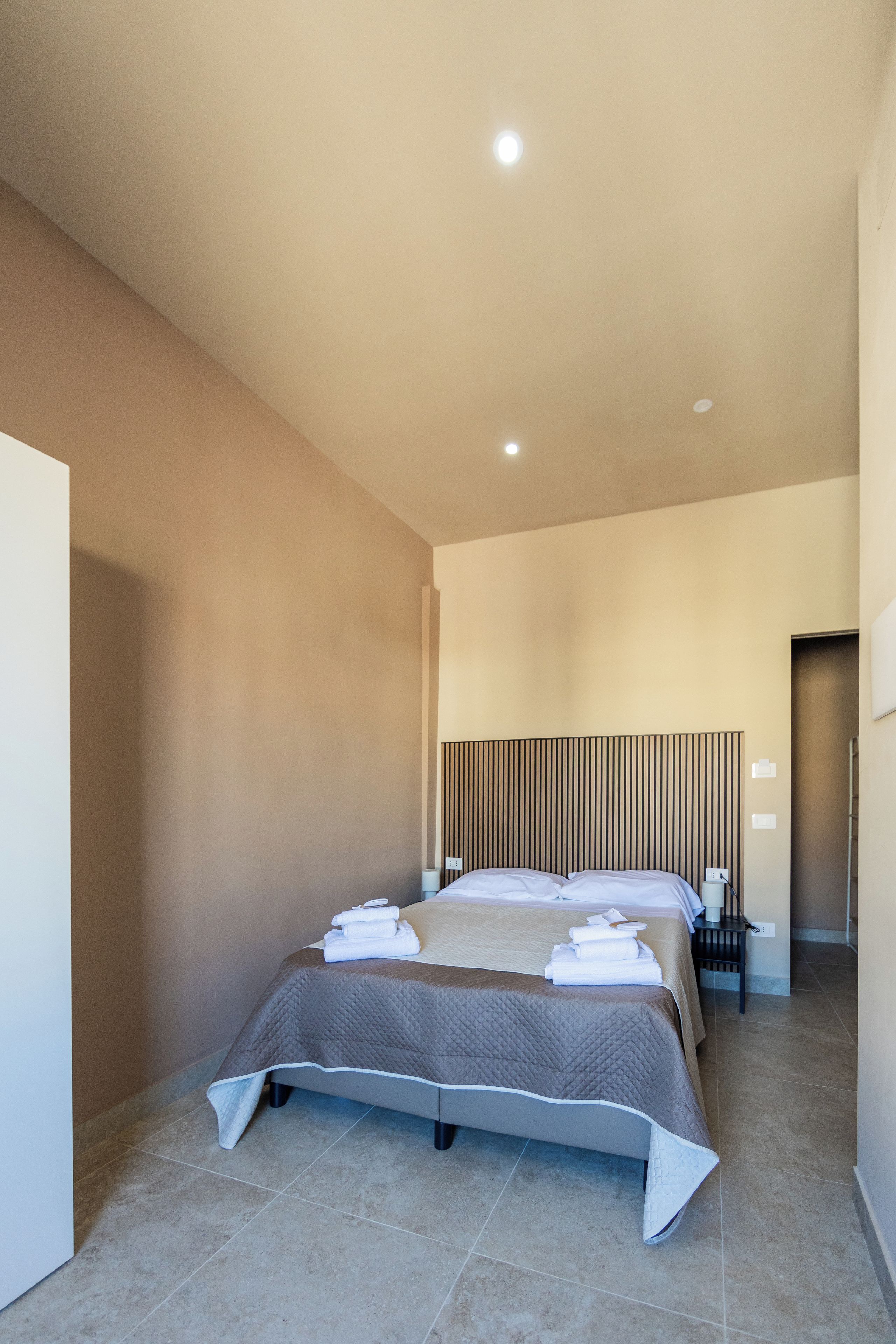 A modern hotel room with two beds, a bedside table, and a headboard with vertical lines.