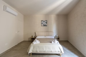 Habitación de hotel minimalista con cama, mesita de noche, aire acondicionado de pared y una obra de arte.