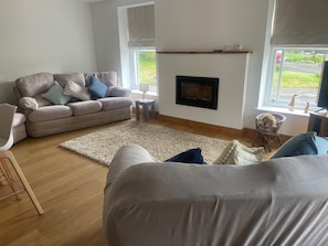 Ein Wohnzimmer mit einer Couch, einem kleinen Tisch, einem Kamin und Blick ins Freie.