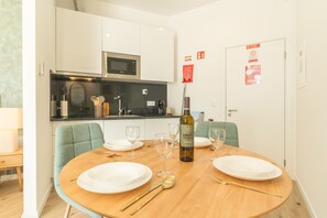 A dining area with a round table set for two, a bottle of wine, and a kitchen in the background. - Rosa Studio by Atlantic Holiday (Santa Cruz)