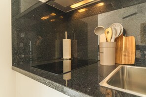 A kitchen with a black granite countertop, stainless steel sink, and a utensil holder with wooden utensils. - Rosa Studio by Atlantic Holiday (Santa Cruz)