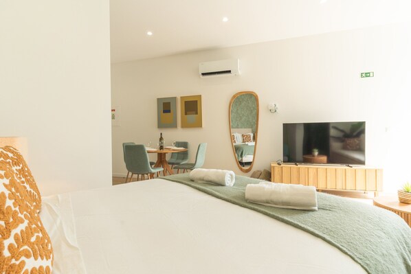 A hotel room with a bed, a TV, a dining area with chairs, and a mirror. - Rosa Studio by Atlantic Holiday (Santa Cruz)