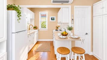 A kitchen with white cabinets, a refrigerator, a window with blinds, a sink, a stove, and two stools.
