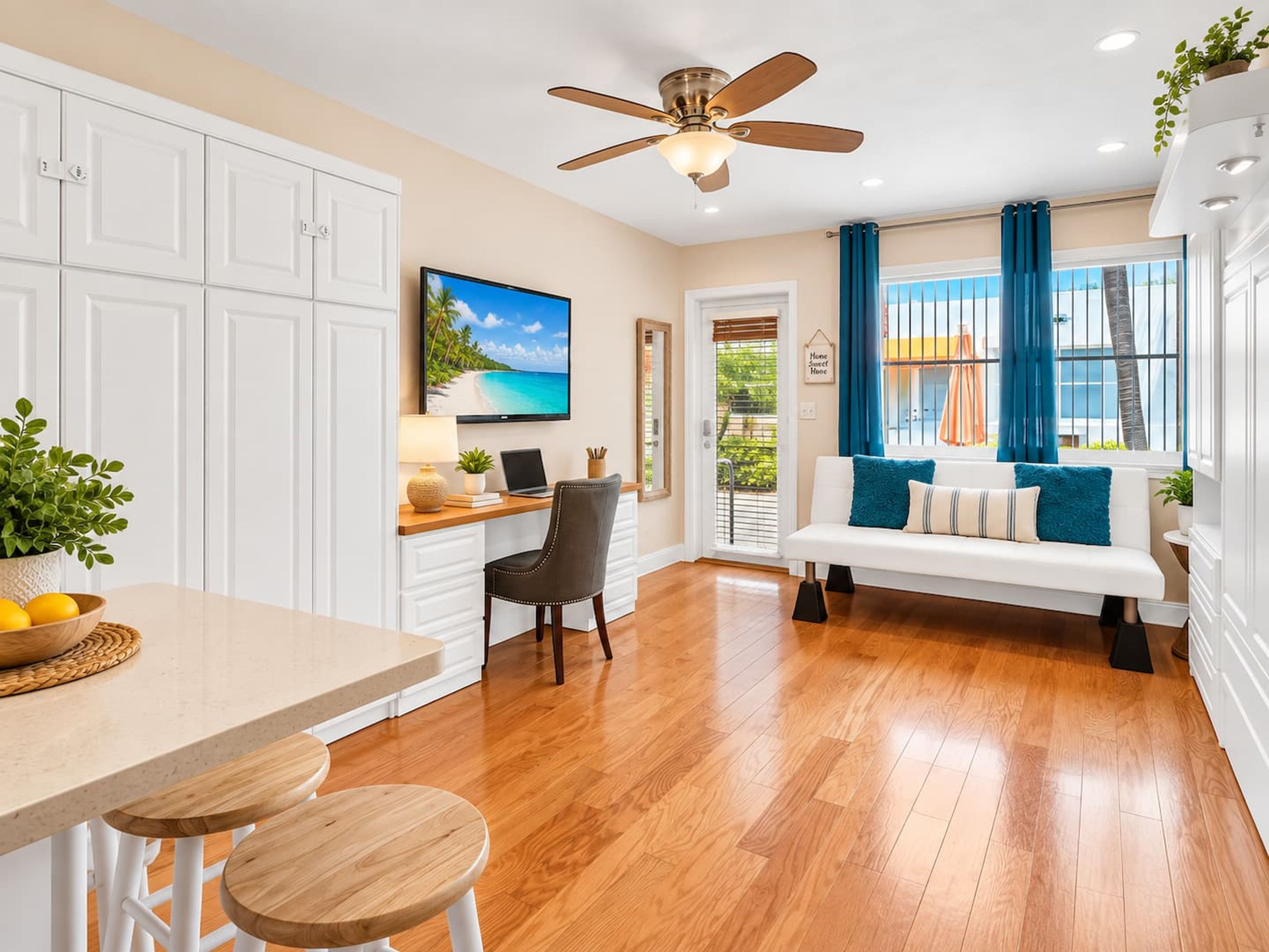 A modern kitchen with white cabinetry, a dining area with a wooden table and chairs, a ceiling fan, and a view of the outdoors through a window with blue curtains.