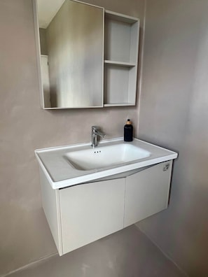 Un bagno con un lavandino bianco, uno specchio e un armadietto.
