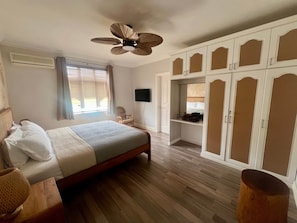 Una camera da letto con un letto, una ventola a soffitto, un armadio, una televisione e una finestra con persiane.