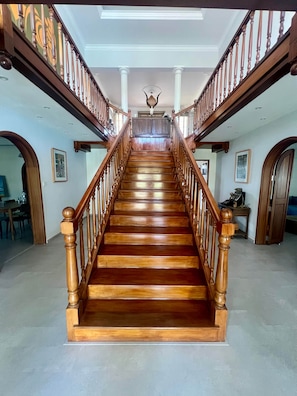 A grand wooden staircase with a balustrade, leading to a landing with a decorative ceiling feature.